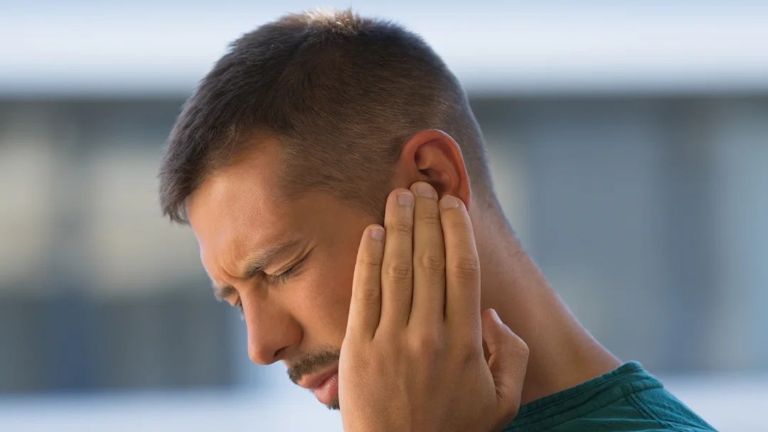 Un homme souffrant, tenant son oreille avec une expression de douleur.