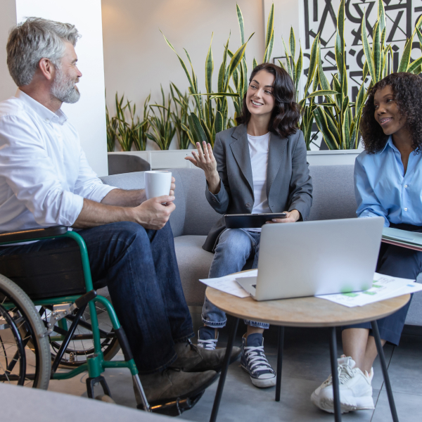 Un homme en fauteuil roulant discute avec deux femmes, illustrant l'innovation sociale et l'inclusion.
