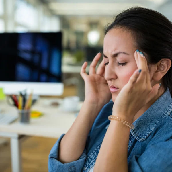 Une femme se tient la tête, exprimant une douleur intense sur son visage.