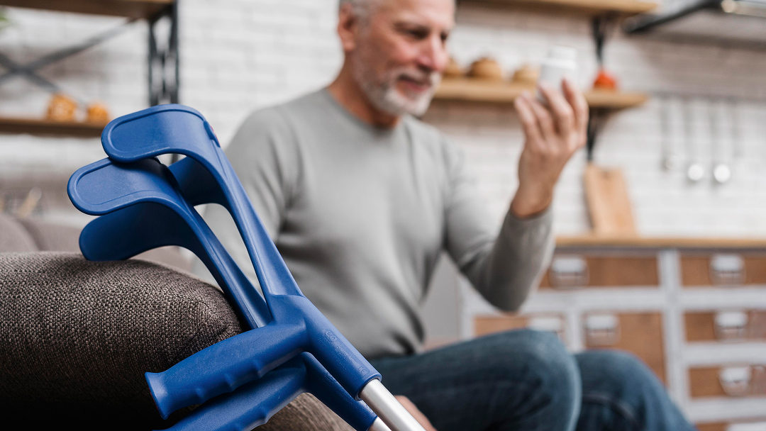 Un homme assis sur un canapé, tenant une béquille bleue, évoquant la question de l'invalidité permanente après 65 ans.