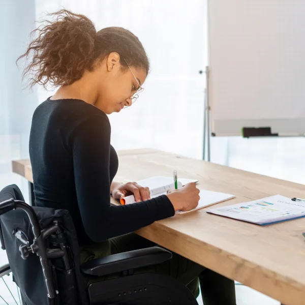 Une femme en fauteuil roulant travaille à un bureau avec un ordinateur portable, utilisant une rente d'invalidité.
