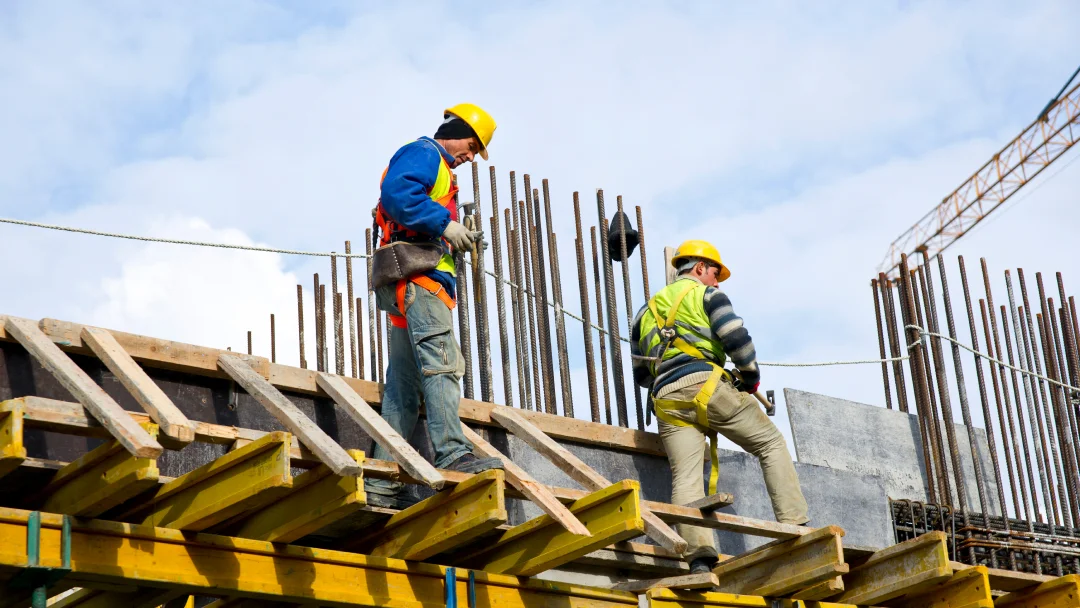 Des ouvriers de construction travaillant sur un chantier, portant des casques et des gilets de sécurité.